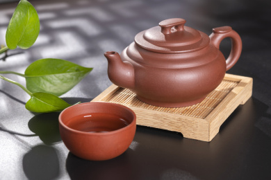 窗影下的黑色桌面上摆放着传统茶具紫砂壶及紫砂杯