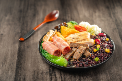 暗色木纹桌面上放着一盘煎牛肉条与鸡胸肉培根黑米饭简餐