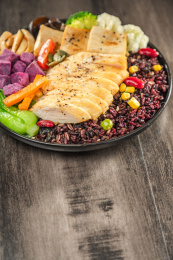 暗色木纹桌面上放着一盘煎鸡胸肉豆腐块黑米饭简餐