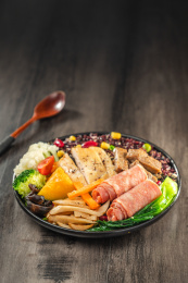 暗色木纹桌面上放着一盘煎牛肉条与鸡胸肉培根黑米饭简餐