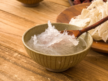 木板上中式陶碗里勺子盛起的燕窝