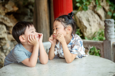 一位可爱的小男孩和一位美丽的小女孩趴在故宫的石桌上托着腮互相对视