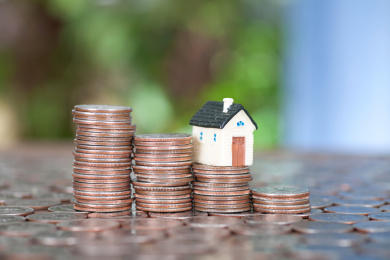 递减的美元硬币和房子模型在铺满硬币的背景上