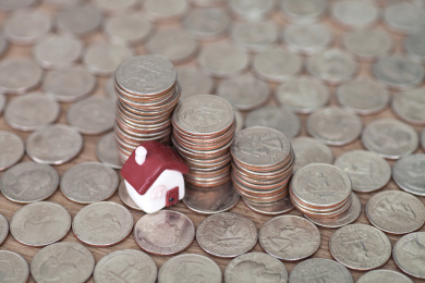 大量美元硬币铺成的背景上一枚袖珍房子模型和一排递减的美元硬币