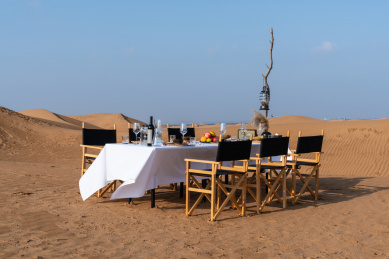 金黄色沙漠中的白色桌布的长条餐桌上的各种美食和木质餐椅