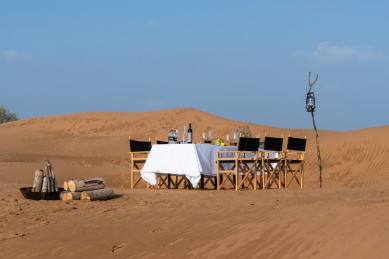 金黄色沙漠中的白色桌布的长条餐桌上的各种美食和木质餐椅