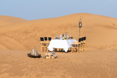 金黄色沙漠中的白色桌布的长条餐桌上的各种美食和木质餐椅