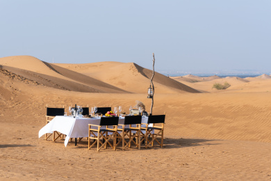 金黄色沙漠中的白色桌布的长条餐桌上的各种美食和木质餐椅