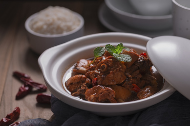 原木质感的桌面上白色砂锅盛着大块的黄焖鸡