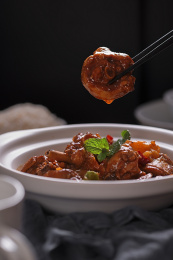 原木质感的桌面上白色砂锅盛着大块的黄焖鸡