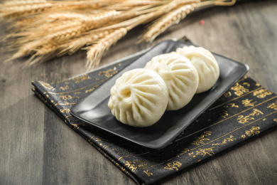 棕色木纹桌面上黑色餐盘里放着三个肉包子
