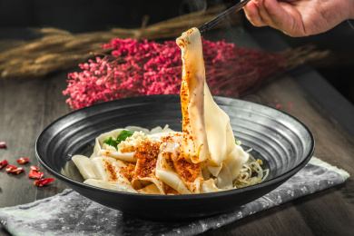 手拿筷子挑起桌上的一碗油泼拌面的面条