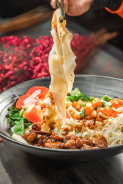 手拿筷子挑起桌上的一碗油泼拌面的面条