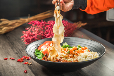 手拿筷子挑起桌上的一碗油泼拌面的面条