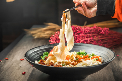 手拿筷子挑起桌上的一碗油泼拌面的面条