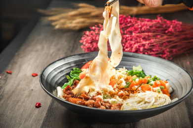 手拿筷子挑起桌上的一碗油泼拌面的面条