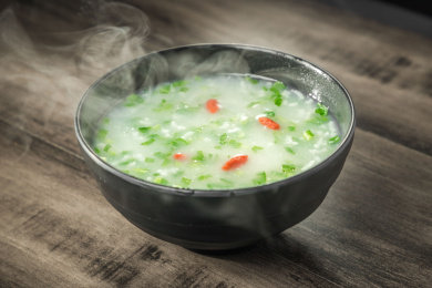 棕色木纹桌面上放着一份冒着热气的菜粥