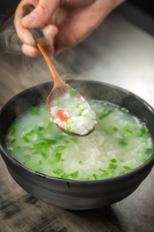 棕色木纹桌面上放着一份冒着热气的菜粥