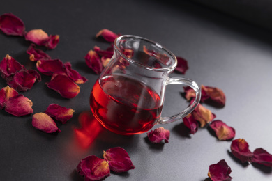 玫瑰茄花茶盛放在玻璃杯中摆放在黑色背景上旁边散落干玫瑰花瓣