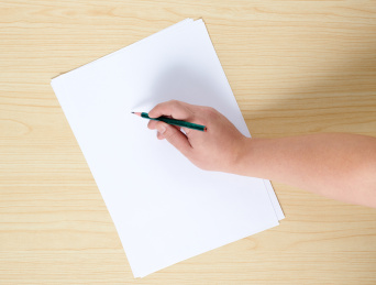 原木桌面上放着一叠白纸,一只手握着铅笔在纸上写字