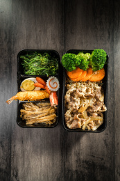 暗色木纹卓上放着一份水煮肥牛日料米饭套餐