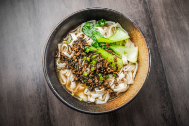 暗色木纹卓上放着一碗雪菜炒肉丁米粉