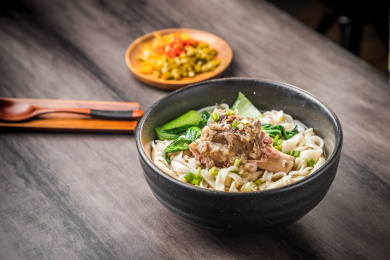 暗色木纹卓上放着一碗高汤顿棒骨米粉