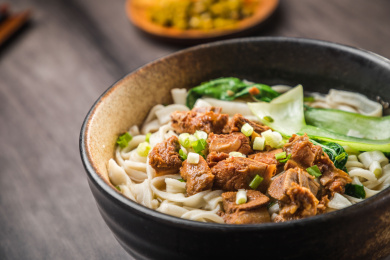 暗色木纹卓上放着一碗炖牛腩米粉