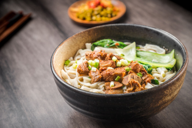 暗色木纹卓上放着一碗炖牛腩米粉