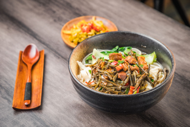 暗色木纹卓上放着一碗猪肉炖豆角米粉