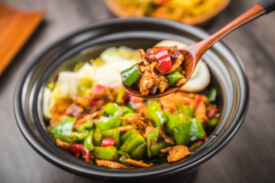 暗色木纹卓上放着一碗青椒小炒肉煲仔饭