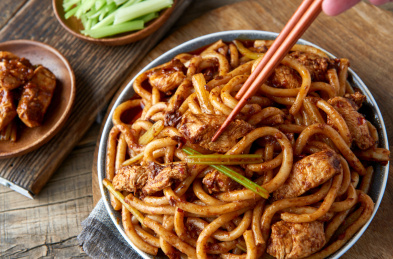 木桌背景下盘中的新疆特色鸡肉炒米粉