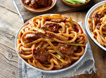 木桌背景下盘中的新疆特色牛肉炒米粉