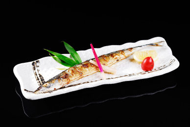 黑色背景浅色瓷盘盛放的香煎秋刀鱼