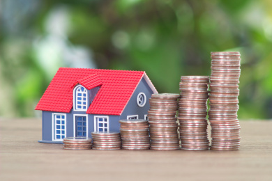 绿植背景前面桌子上递增的美元硬币和房屋模型