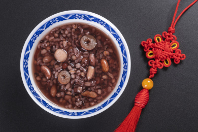 腊八粥与腊八米盛放在青花餐具中摆放在黑色背景上旁边摆放中国结