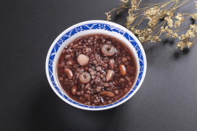 腊八粥与腊八米盛放在青花餐具中摆放在黑色背景上旁边摆放中国结