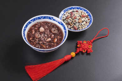 腊八粥与腊八米盛放在青花餐具中摆放在黑色背景上旁边摆放中国结