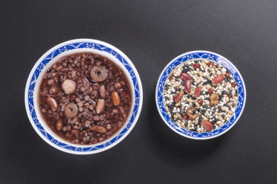 腊八粥与腊八米盛放在青花餐具中摆放在黑色背景上旁边摆放中国结