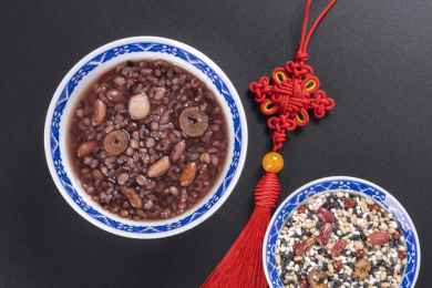 腊八粥与腊八米盛放在青花餐具中摆放在黑色背景上旁边摆放中国结