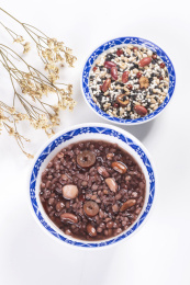 腊八粥与腊八米盛放在青花餐具中摆放在黑色背景上旁边摆放中国结