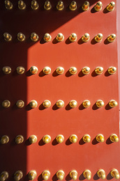 光影下的红色宫门上镶嵌着金黄色的门钉