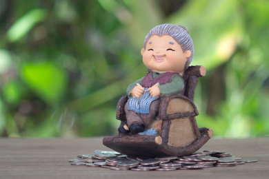 放在一堆美元硬币上坐着摇椅的老太太模型