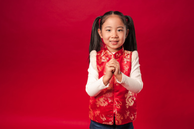 站在红色背景前穿唐装马甲作揖的中国女孩