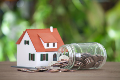 桌子上的小房子模型和歪倒并散出美元硬币的玻璃瓶