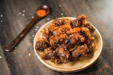 暗色木纹桌上放着一盘撒着辣椒面的油炸鸡心