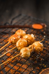 黑色烤架上放着几串撒着辣椒面的油炸鱼丸