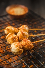 黑色烤架上放着几串撒着辣椒面的油炸鱼丸