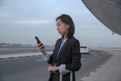 在路边带着行李箱使用智能手机打车的女白领