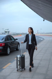 刚下车的一位商务女士拿着拉杆箱走在马路上